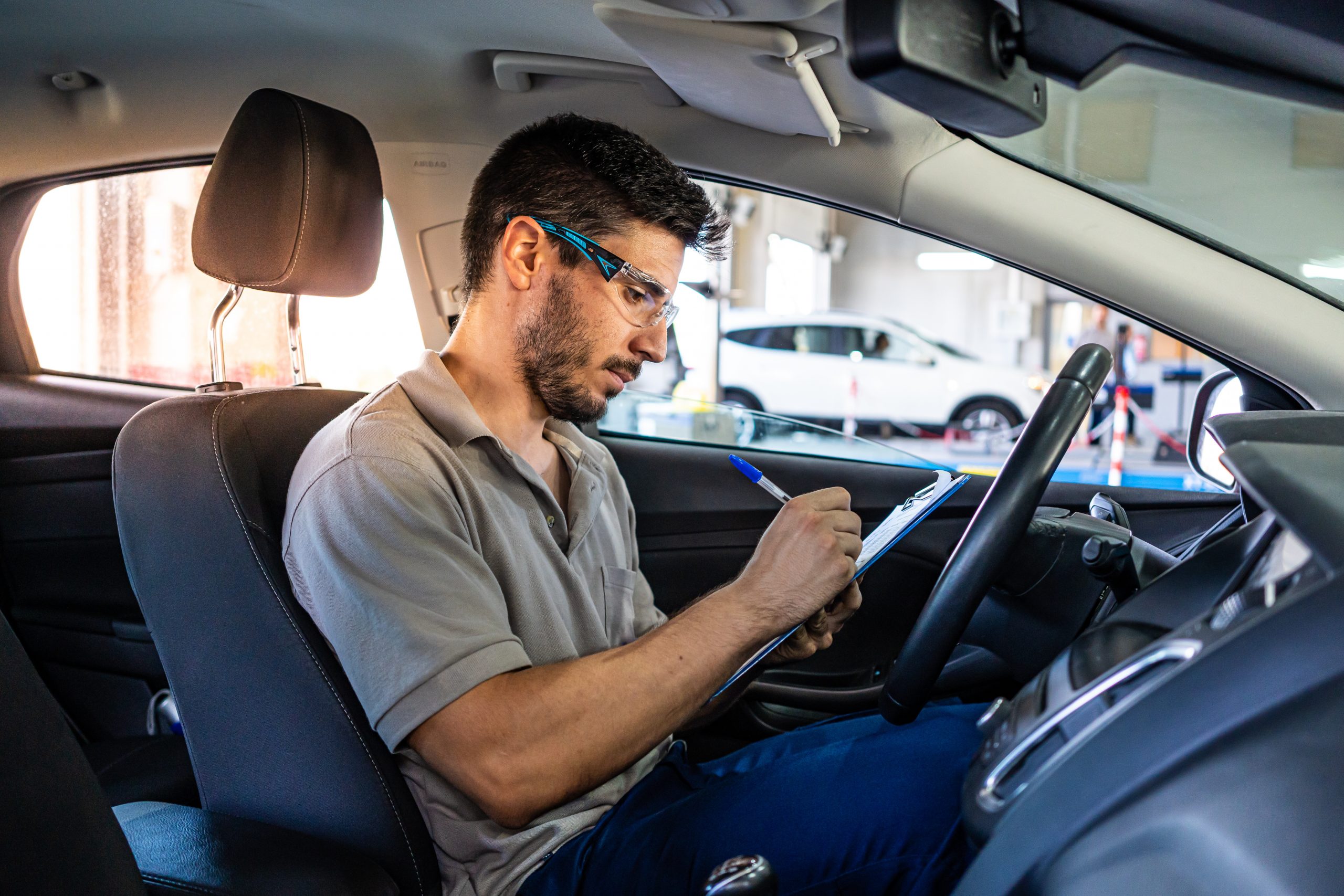Technician with safety glasses sitting in a car seat checking a list during a vehicle inspection